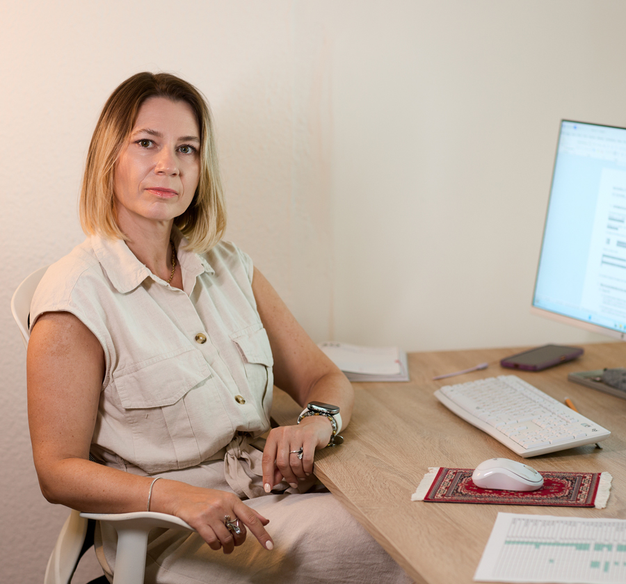 Fotografía de ALEKSANDRA sentada en su puesto de trabajo, se ve también la mesa con el ordenador
